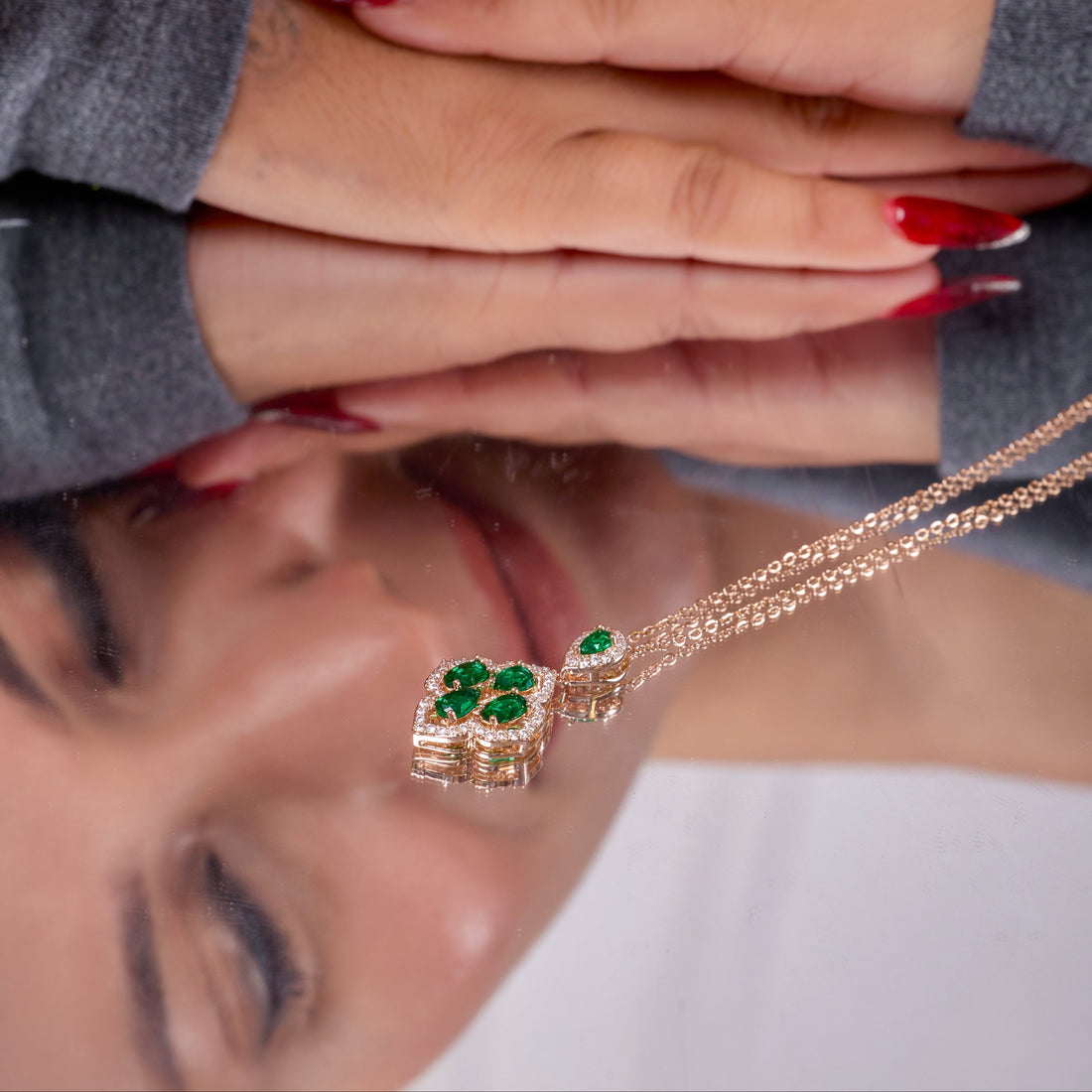 Close-up of a woman's face with a necklace featuring green gemstones, reflected on a surface.