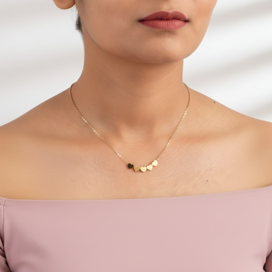 Gold necklace with heart-shaped pendants worn by a person against a neutral background