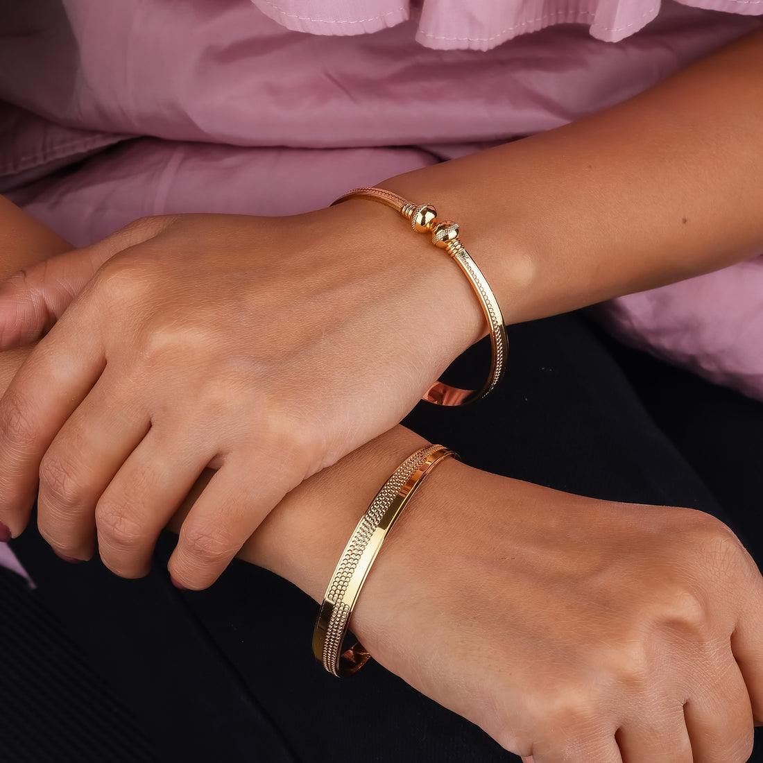 Close-up of hands wearing gold bracelets on a pink background